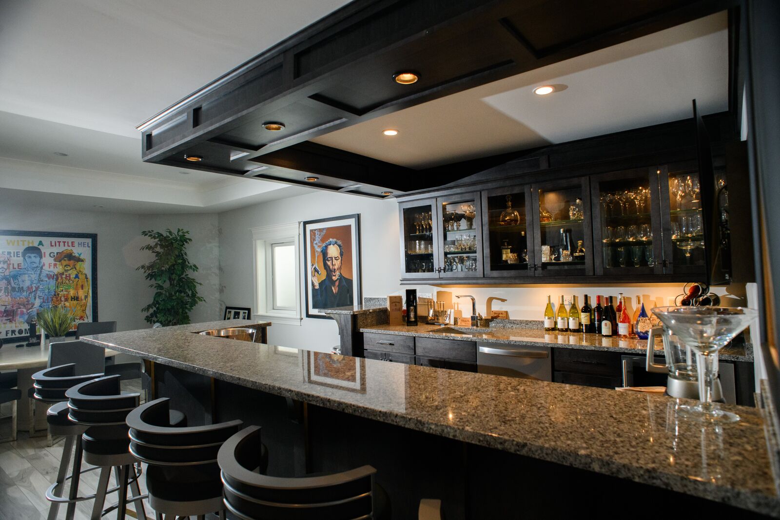 Lower level bar with a granite counter, dark stained cabinetry, glass front upper cabinets and a coffered wood ceiling detail