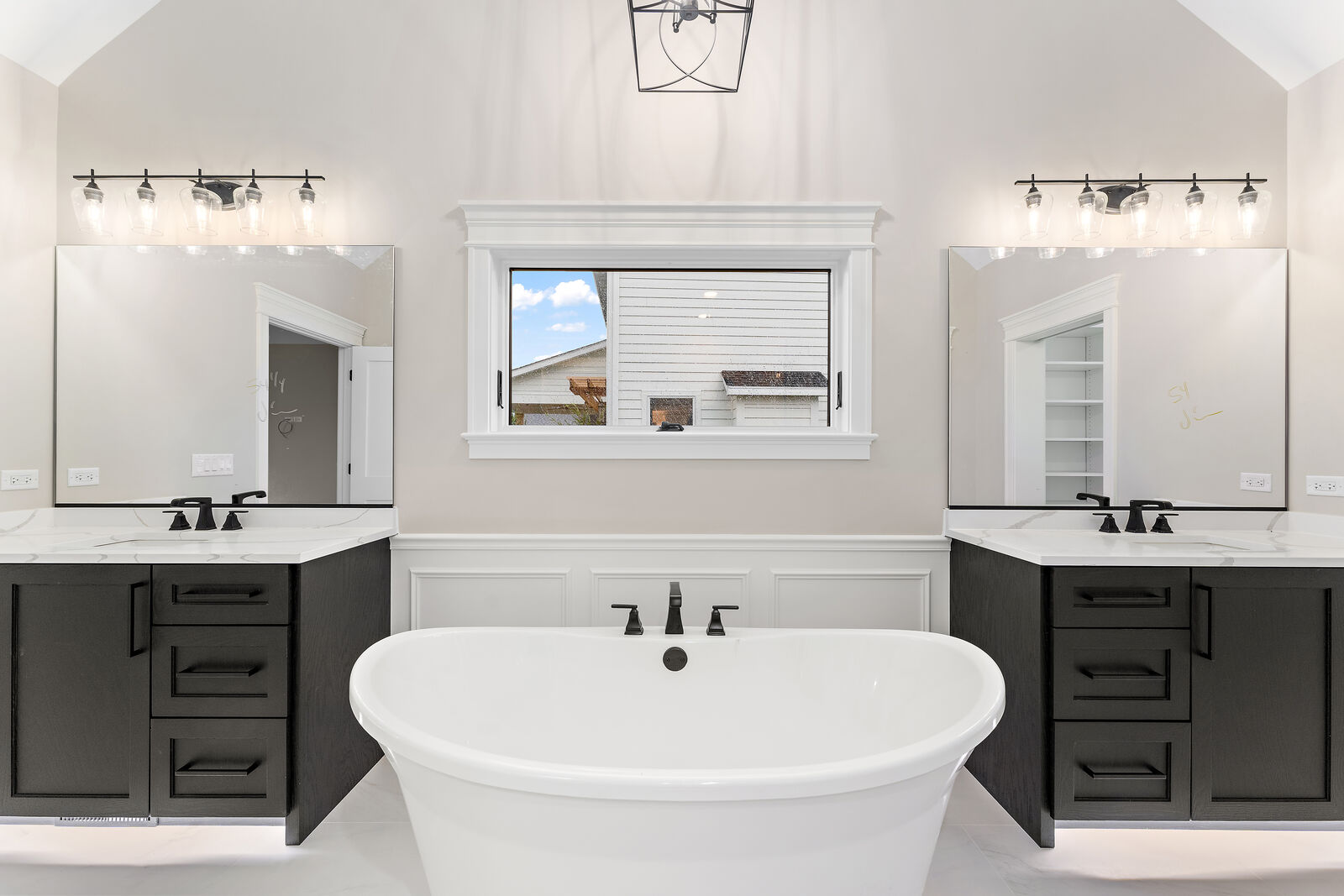 Primary bath with a freestanding soaking tub between two dark vanities under a vaulted ceiling