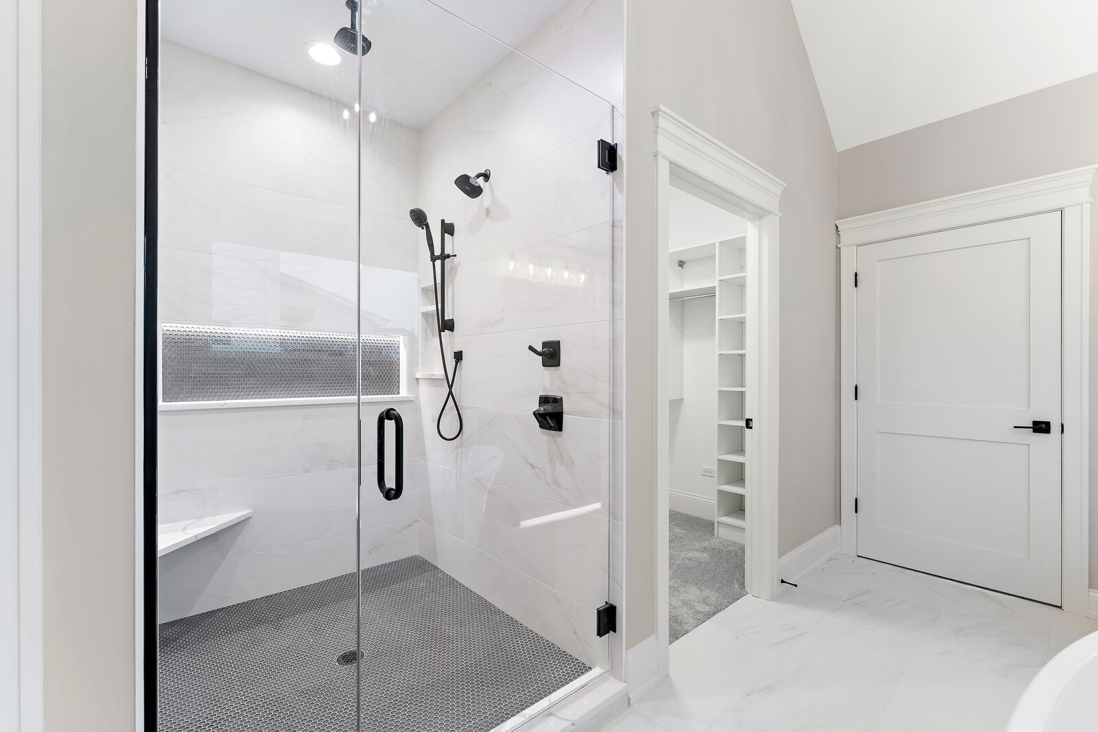 Walk in marble tile shower with a penny tile floor, glass door and built in bench