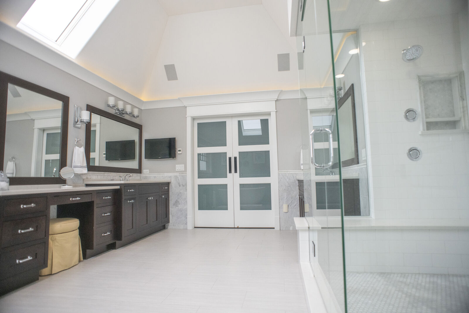 Primary bath with a long double vanity, framed mirrors and a skylit vaulted ceiling