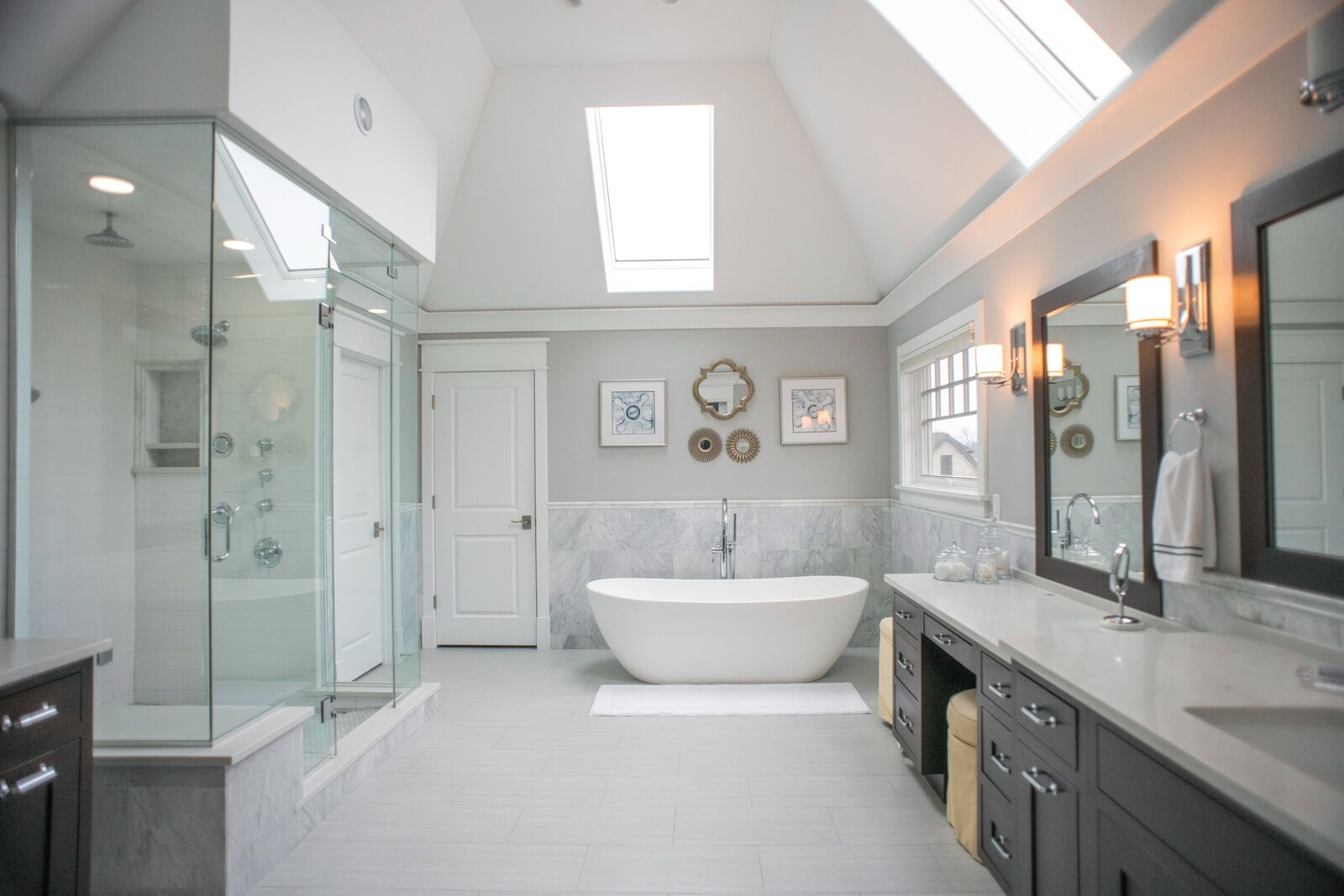 Primary bath with a freestanding tub, marble tile wainscot, skylit vaulted ceiling and a glass walk in shower