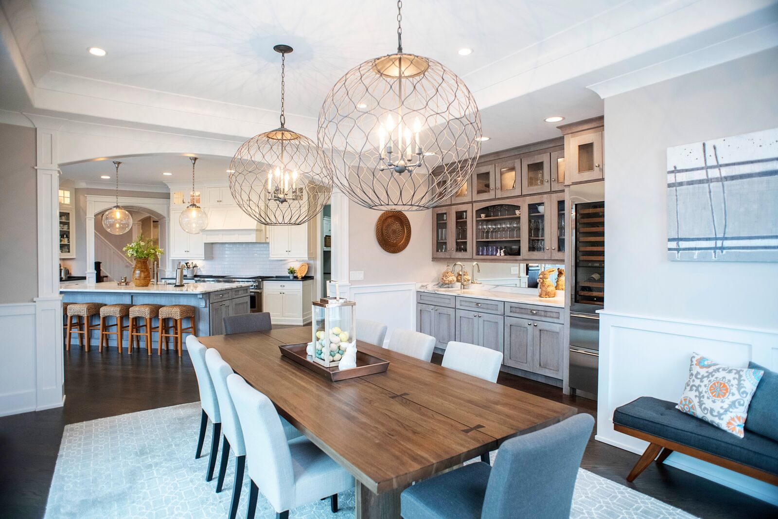 Dining area with globe chandeliers and a built in wet bar with glass front cabinetry, wine refrigerator and stone counter, open to the kitchen