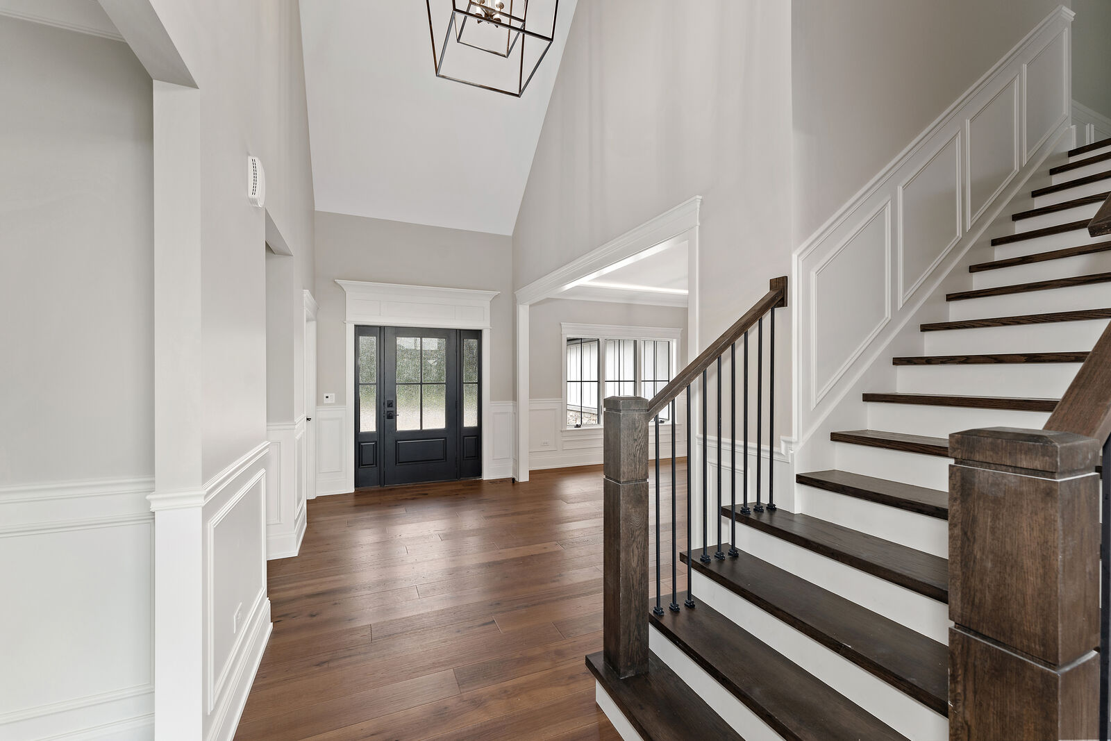 Two story entry with a black glass front door, wainscoting and a stained staircase with iron balusters