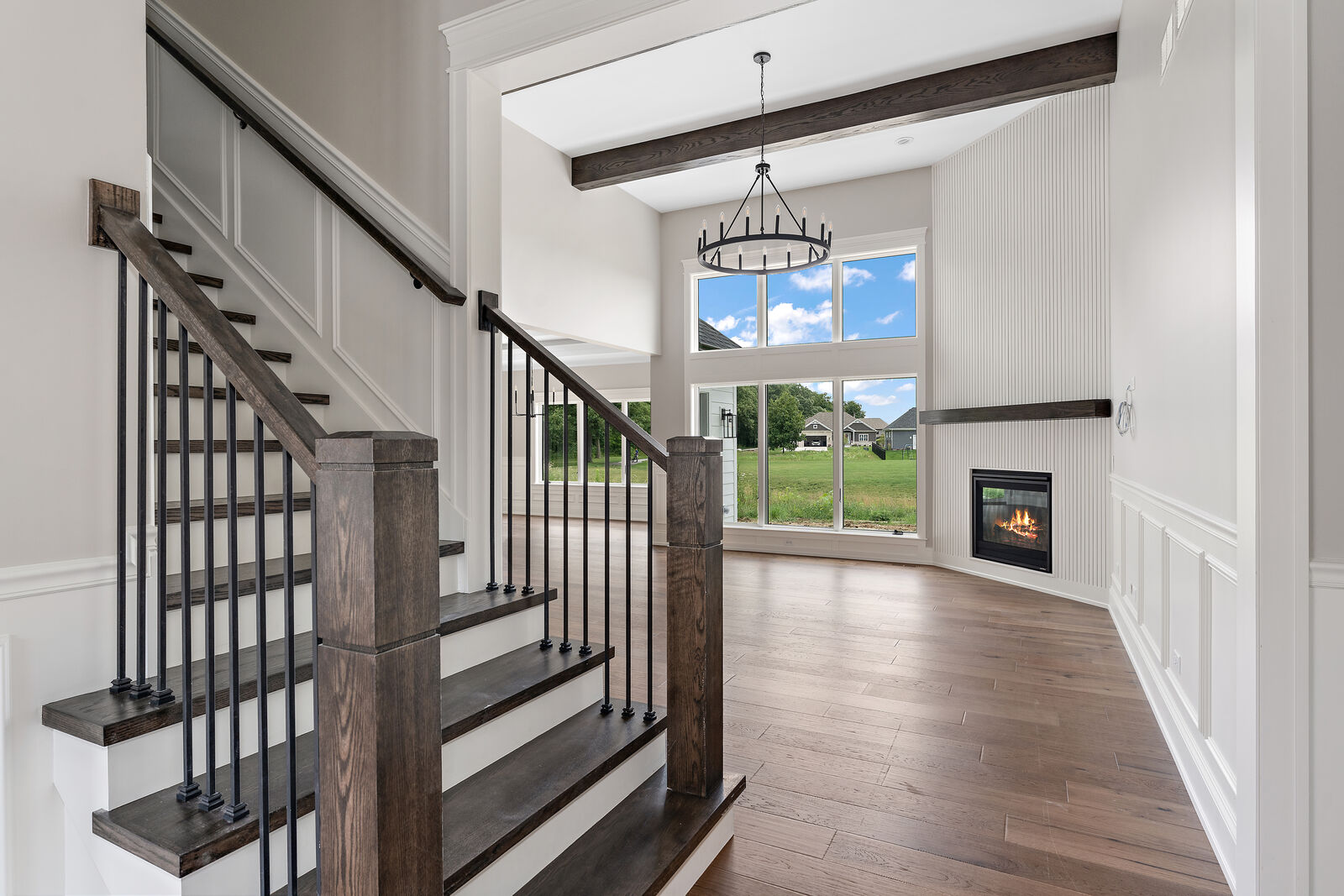 Staircase with stained handrail and iron balusters looking into a beamed great room with a fireplace