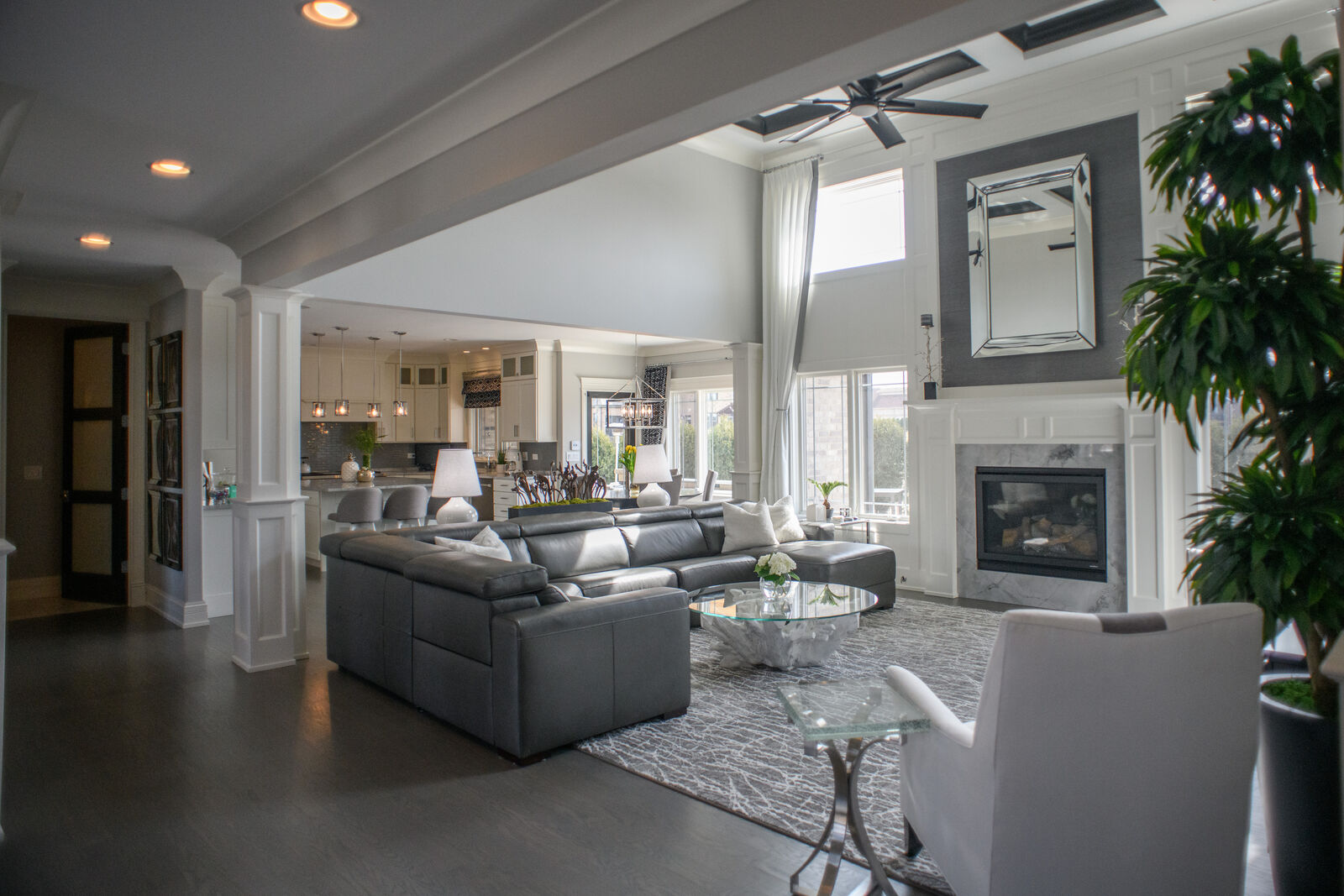 Open concept great room with a marble fireplace, coffered detailing and a view through to the kitchen
