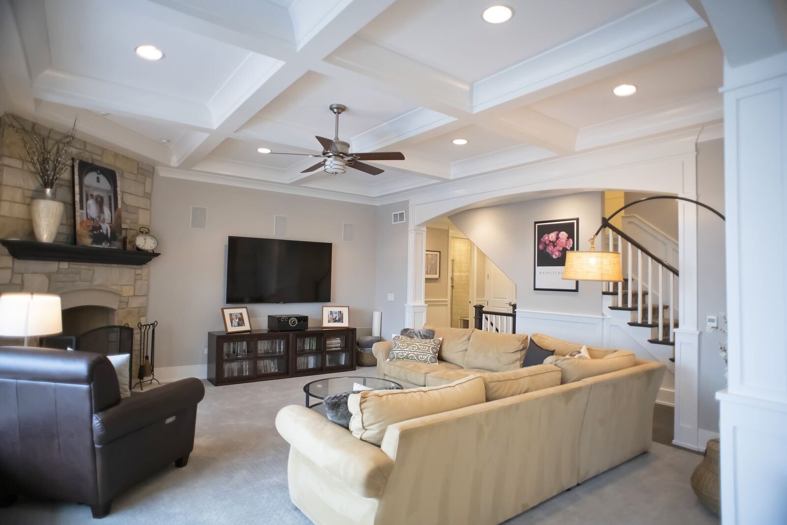 Family room with a coffered ceiling, stone fireplace with a dark wood mantel and an arched opening to the stairway