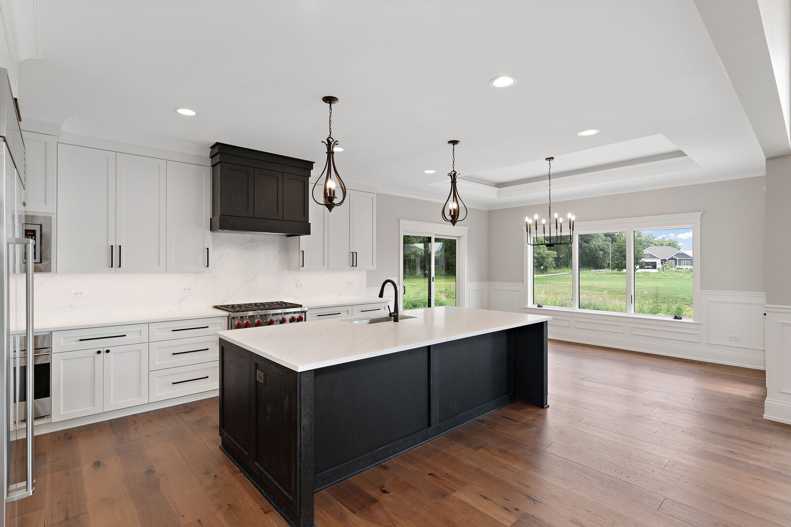 Custom kitchen with white cabinetry, a black stained island, quartz waterfall backsplash and a dark wood range hood