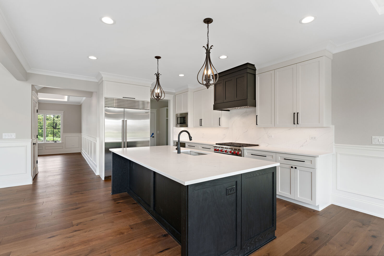 Wide view of a custom kitchen with black island, professional range and marble-look quartz backsplash