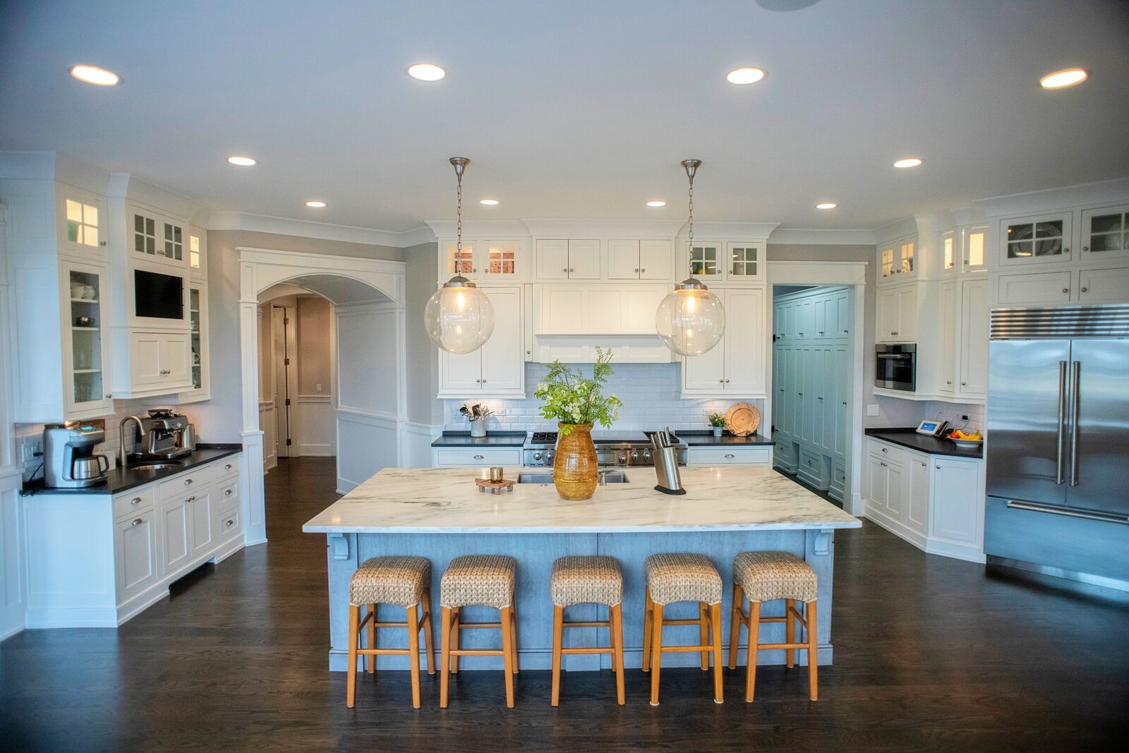 White custom kitchen with a marble-topped island, glass globe pendants and a painted blue pantry