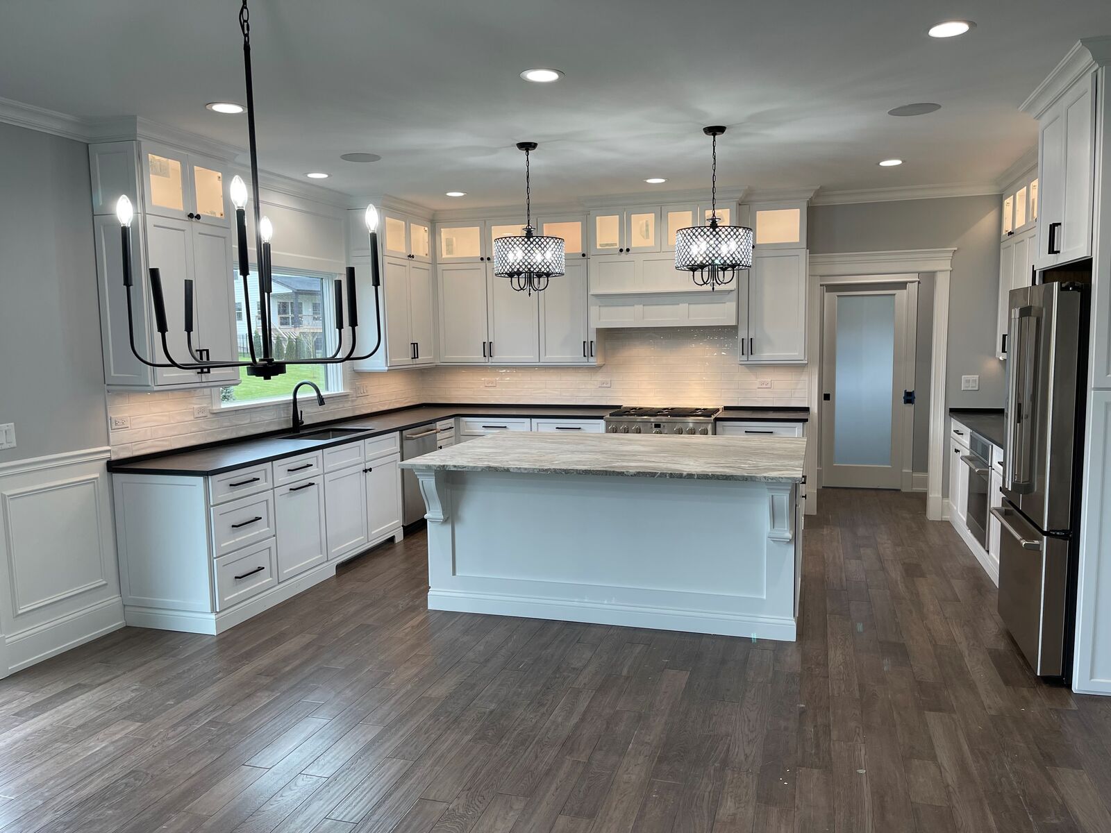 White custom kitchen with a stone topped island, black countertops, subway tile backsplash and a frosted glass pantry door