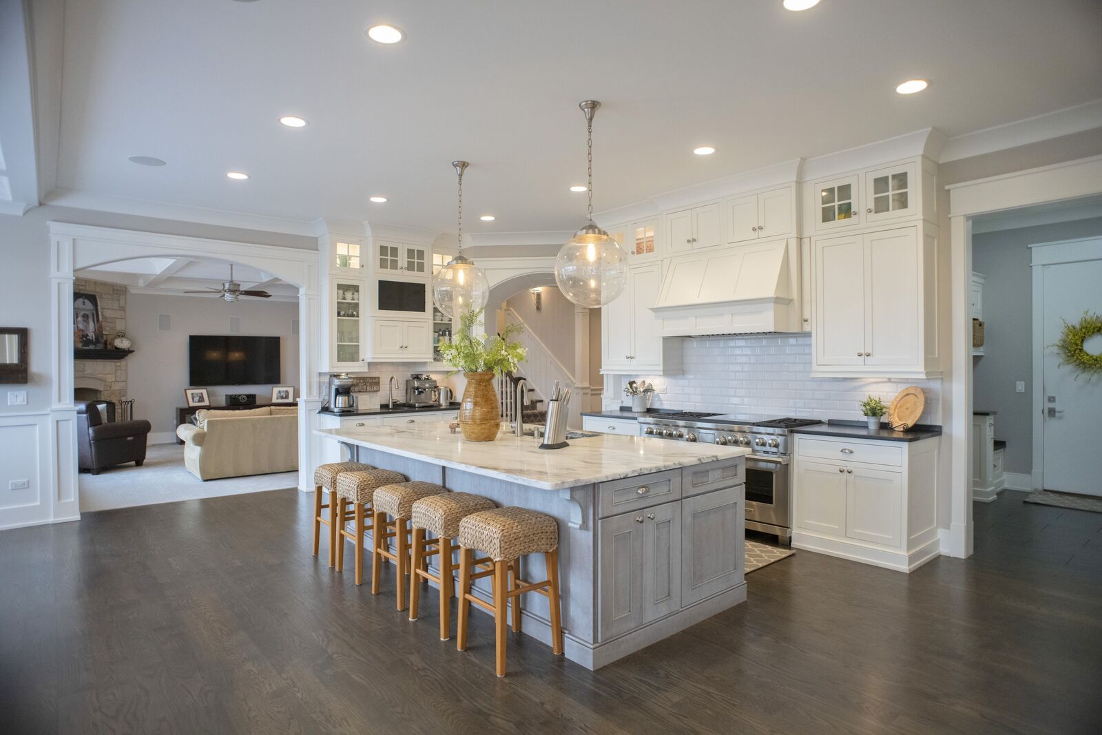 Custom kitchen with a marble topped island, white cabinetry and subway tile, open to the family room beyond