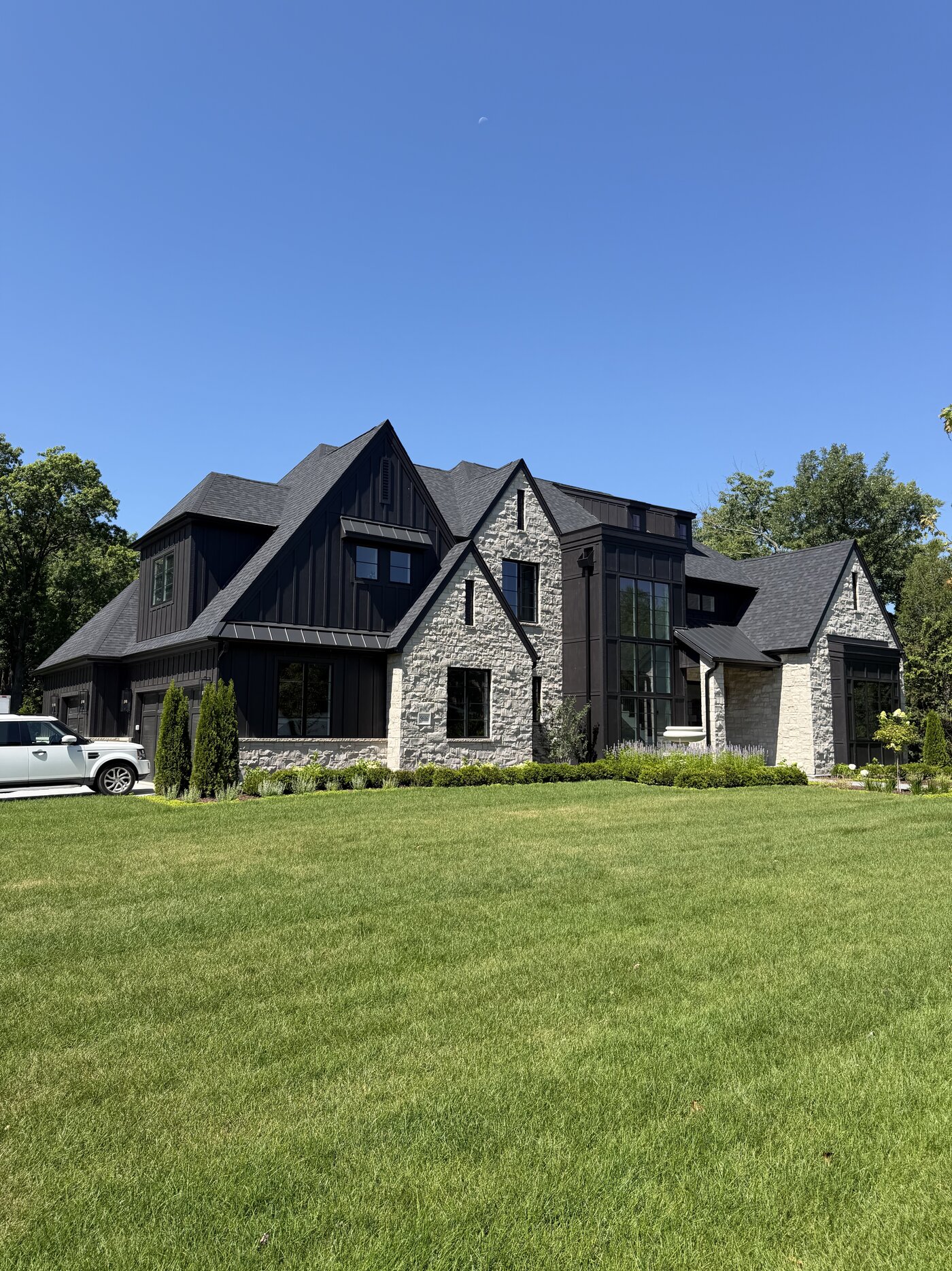 Modern Tudor custom home with black board-and-batten siding, white limestone and a glass stair tower built by Spyglass